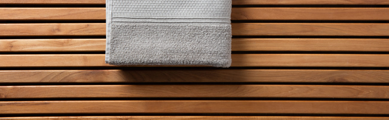 Half grey towel for spa, hammam, sauna, shower, bath, hygiene or body care concept with grey cotton towel set over beautiful wooden board, copy space long banner